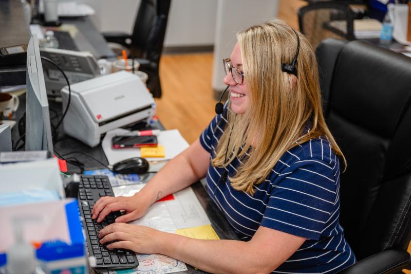 a woman with a headset smiling at a computer