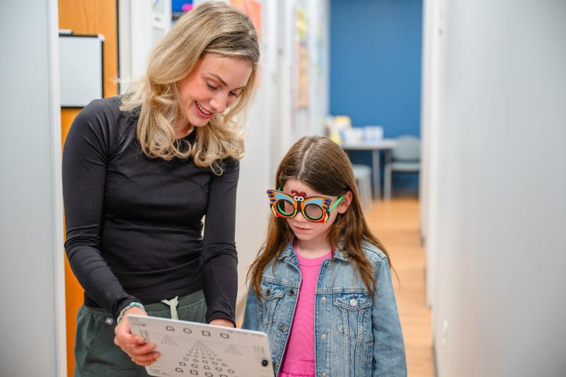 a girl wearing crazy glasses looking at a paper with an adult